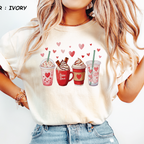 Ivory Comfort Colors t-shirt featuring a watercolor illustration of four Valentine's Day coffee drinks including a pink frappe and iced coffee.